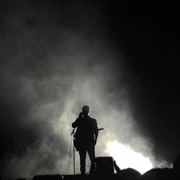 singer is standing on stage under the smogg